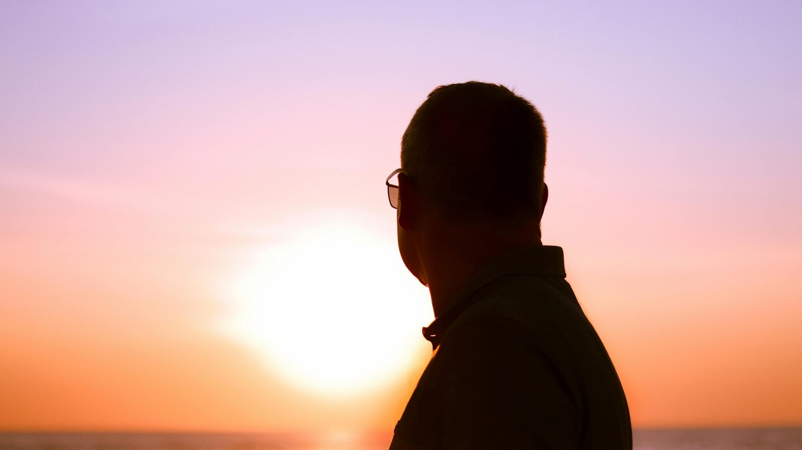 Silhouette of a man in glasses watching a vibrant sunset over the sea in Denmark.